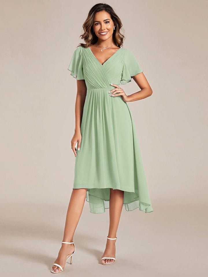 Robe vert sauge portée de face par une mannequin, main sur la hanche, col en V plissé et ourlet asymétrique. 76