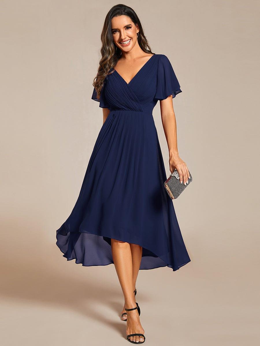 Robe bleu marine en mousseline portée de face par une mannequin souriante, pochette scintillante à la main, ourlet asymétrique. 1