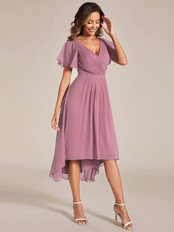 Robe mauve rosé portée de trois quarts par une mannequin, ourlet asymétrique plus long derrière et manches courtes volantées. 62