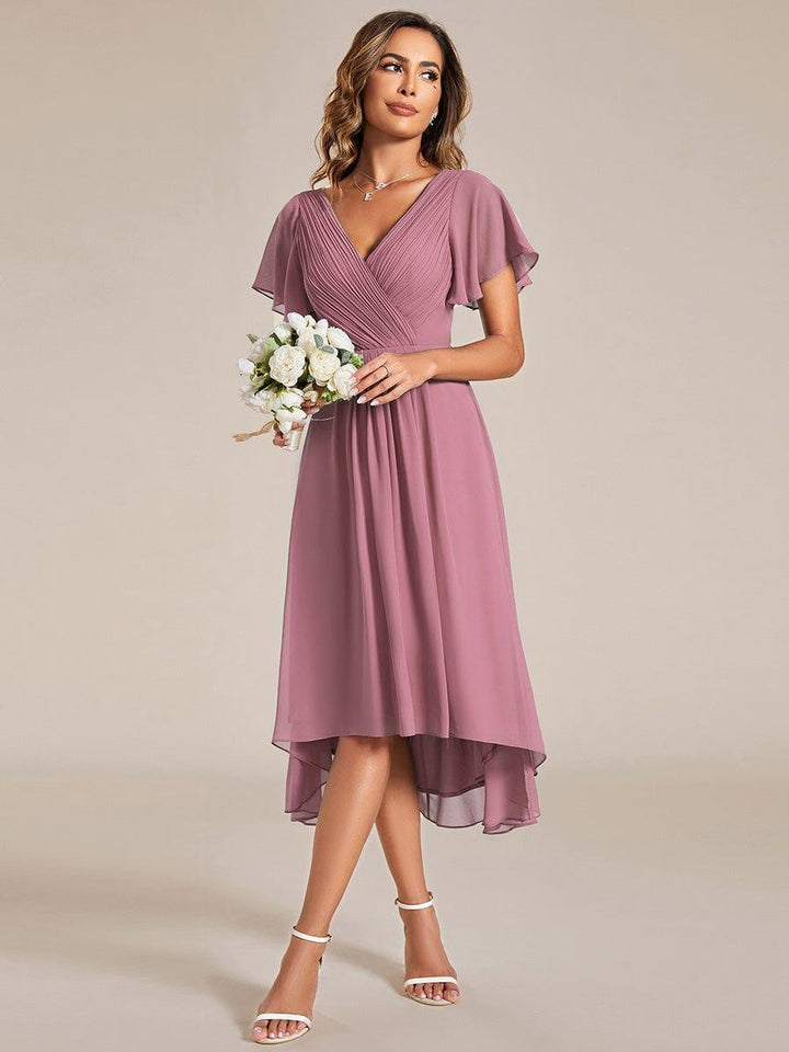 Robe rose mauve portée par un mannequin tenant un bouquet de fleurs blanches, sandales blanches, jupe asymétrique en mousseline. 60