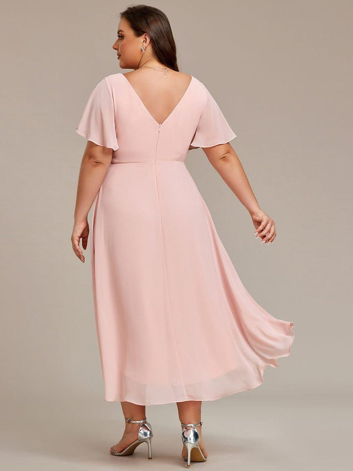 Robe rose pâle grande taille vue de dos, décolleté en V, fermeture éclair centrale et jupe asymétrique qui flotte. 32