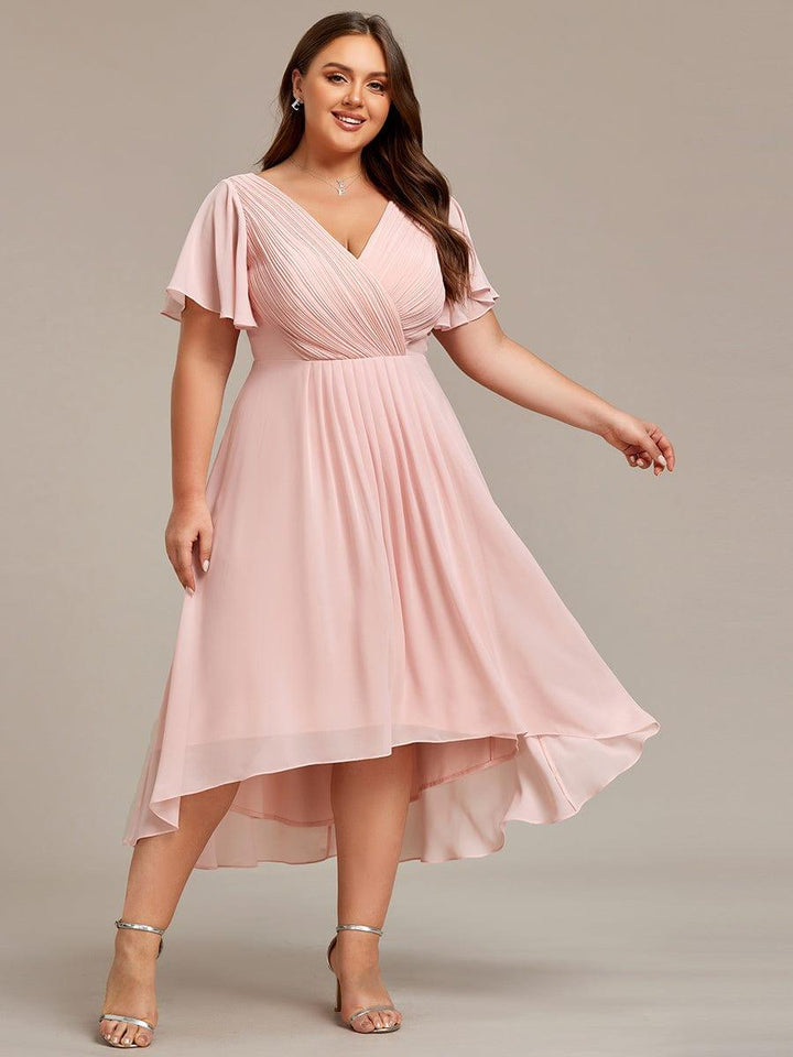 Robe rose pâle grande taille portée de face, mannequin souriante, jupe fluide en mousseline à ourlet asymétrique. 34