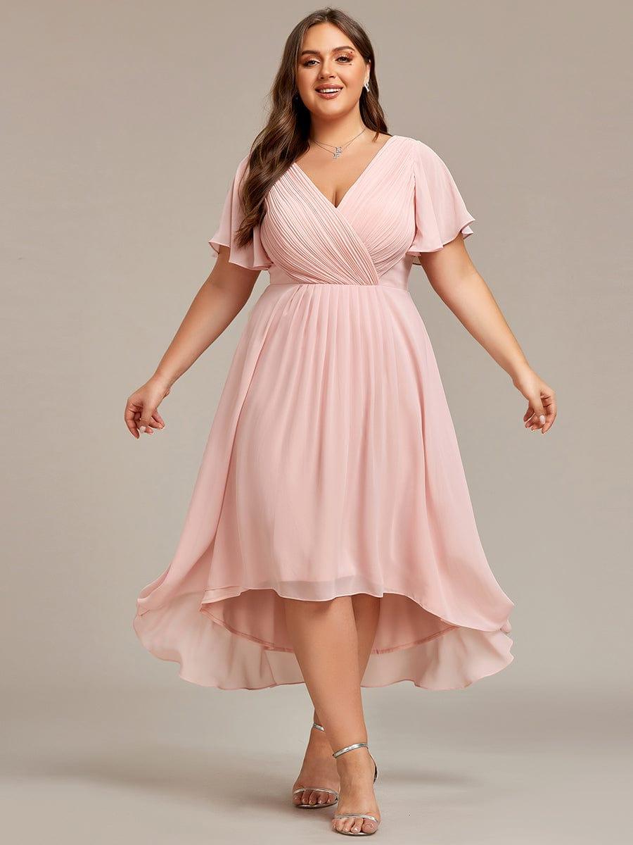 Robe rose pâle grande taille, mannequin les bras écartés, jupe plissée en mousseline à ourlet asymétrique et sandales argentées. 35