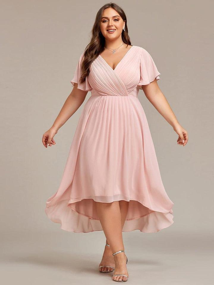 Robe rose pâle grande taille, mannequin les bras écartés, jupe plissée en mousseline à ourlet asymétrique et sandales argentées. 35