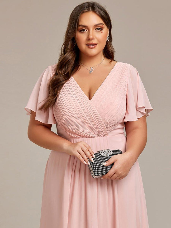 Gros plan sur le corsage plissé croisé de la robe rose pâle, manches volantées, mannequin tenant une pochette scintillante. 33
