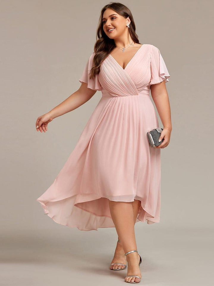 Robe rose pâle grande taille portée par une mannequin en mouvement, pochette scintillante à la main et sandales argentées. 31