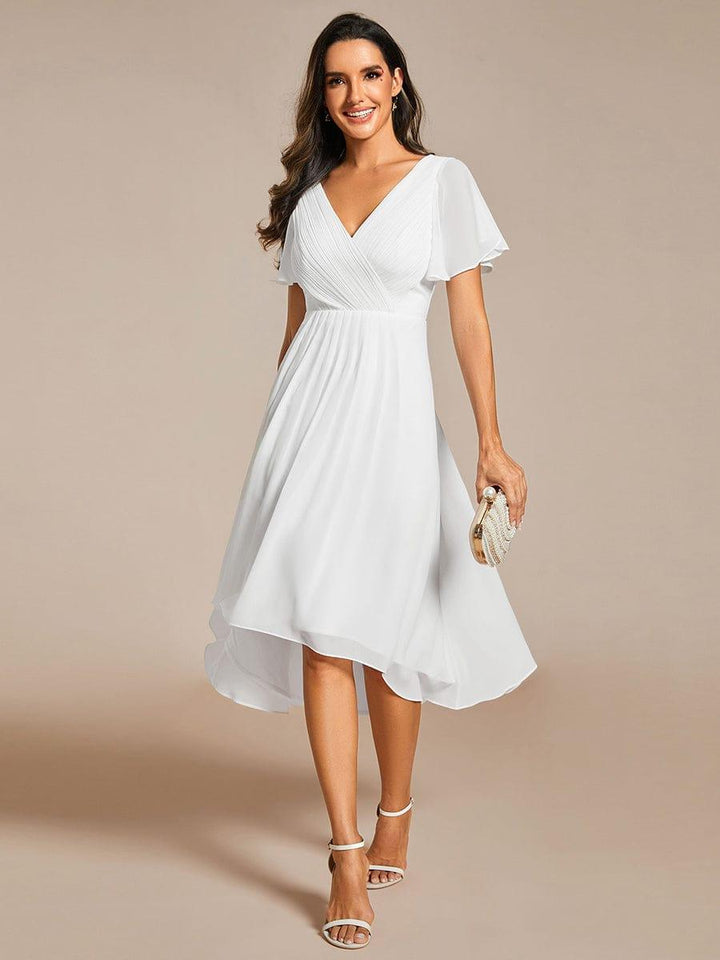 Robe blanche portée de face par une mannequin tenant une pochette perlée, col en V plissé et ourlet asymétrique. 68