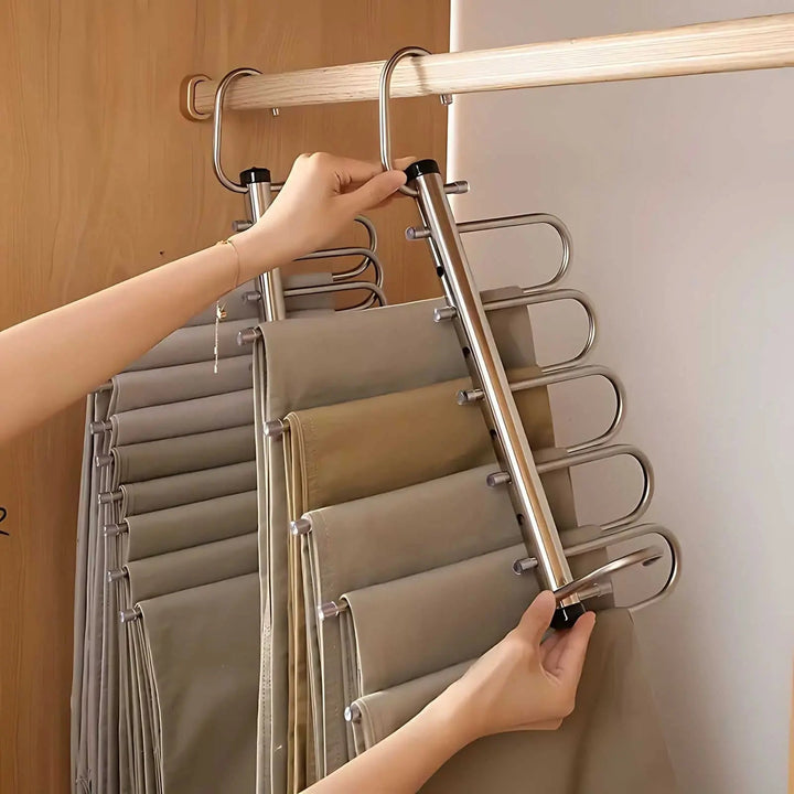 Vue de côté d'une main qui écarte les barres métalliques de l'organisateur pour accéder aux pantalons rangés dans l'armoire. 3