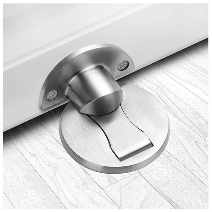 Butée magnétique en métal brossé argenté, fixée au bas d'une porte blanche, socle rond posé sur un parquet clair. 1