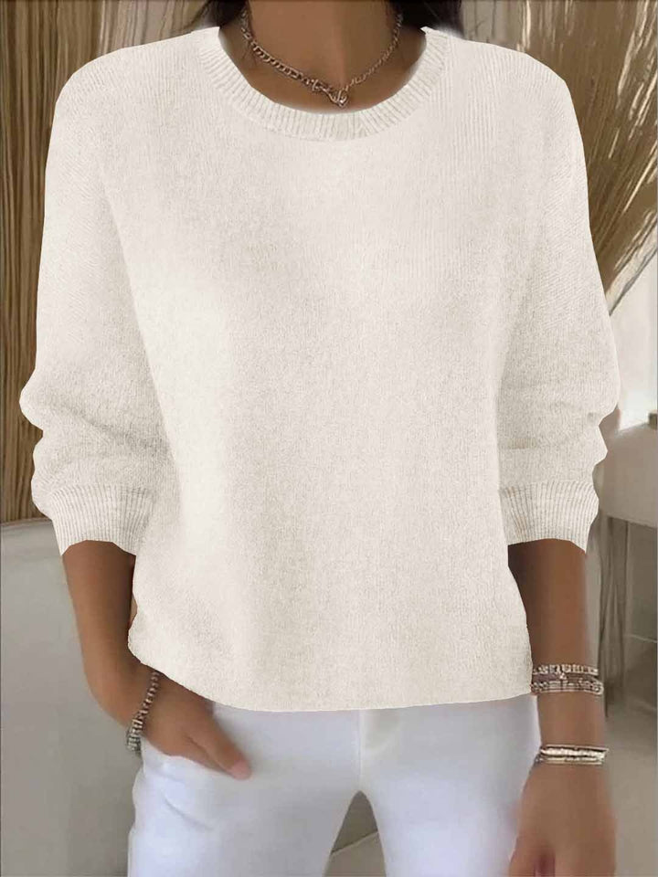 Pull blanc cassé à col rond, porté avec un pantalon blanc, bracelets et collier 4