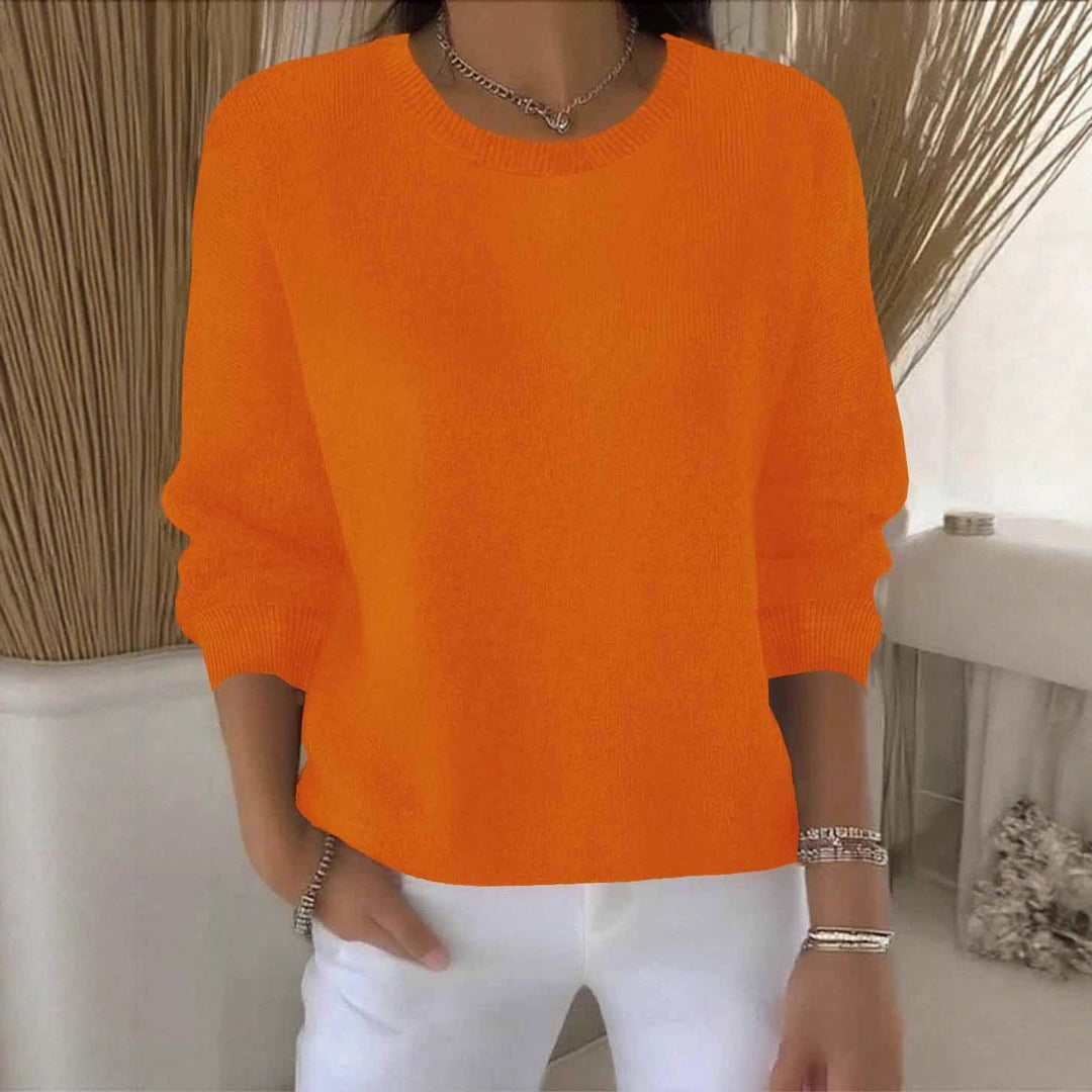 Pull orange vif à col rond, porté avec un pantalon blanc dans un intérieur clair 11