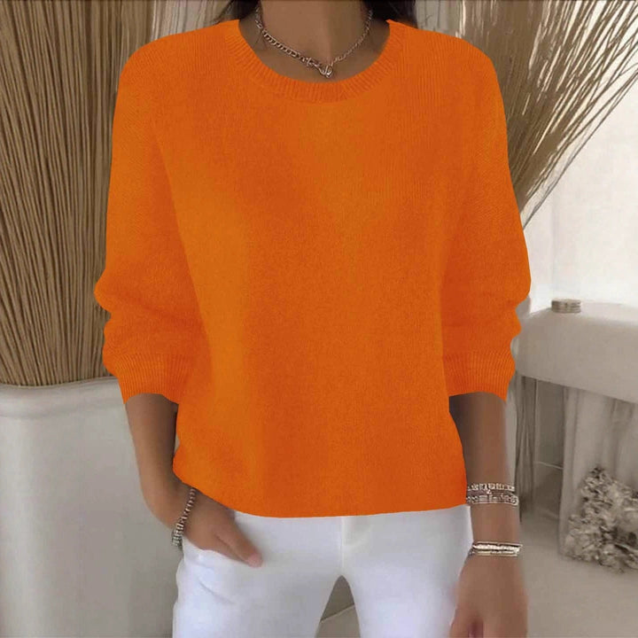 Pull orange vif à col rond, porté avec un pantalon blanc dans un intérieur clair 11