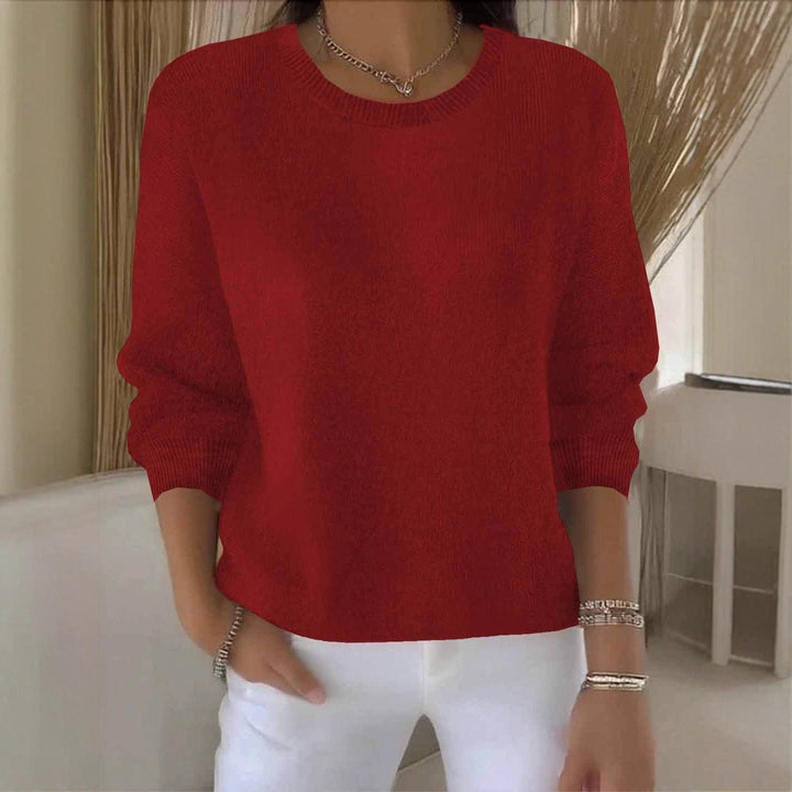 Pull rouge à col rond porté avec un pantalon blanc et des bijoux argentés, fond beige 1
