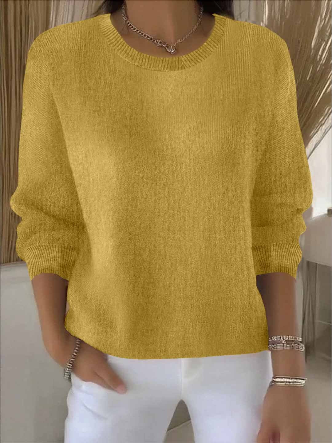 Pull jaune moutarde à col rond, porté avec un pantalon blanc et des bracelets 8