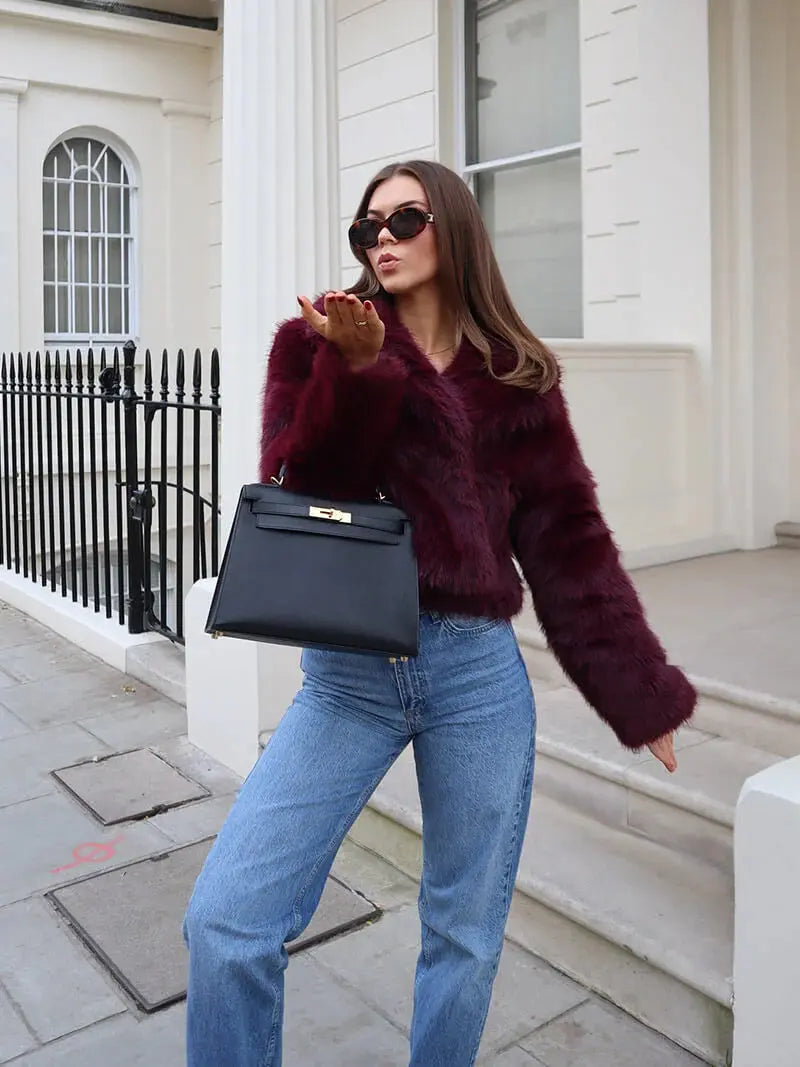 Femme en jean envoyant un baiser, portant le manteau bordeaux en fausse fourrure avec un sac noir à la main 12