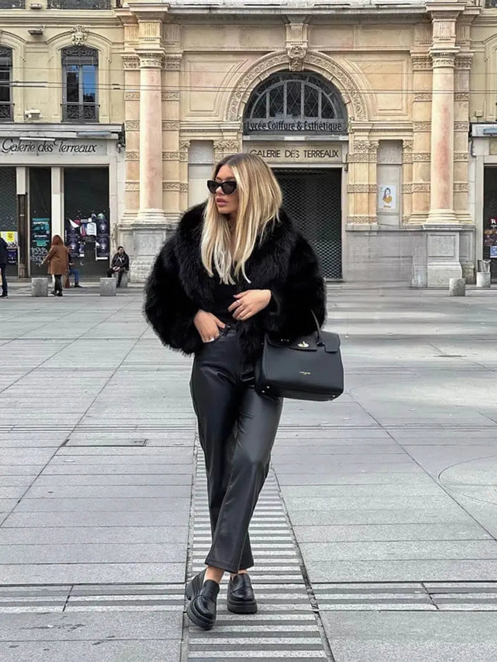 Femme en pied sur une place, manteau noir en fausse fourrure, pantalon en cuir noir et sac à main noir 8