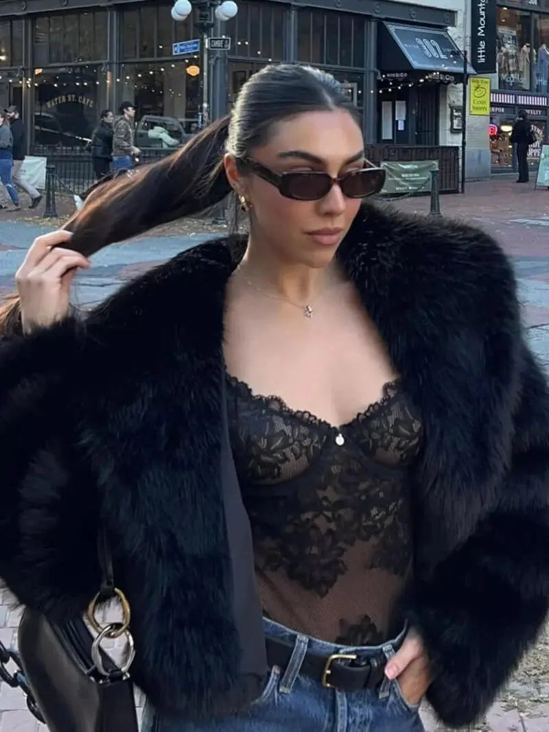 Gros plan sur une femme portant le manteau noir en fausse fourrure ouvert sur un body en dentelle noire et un jean 9