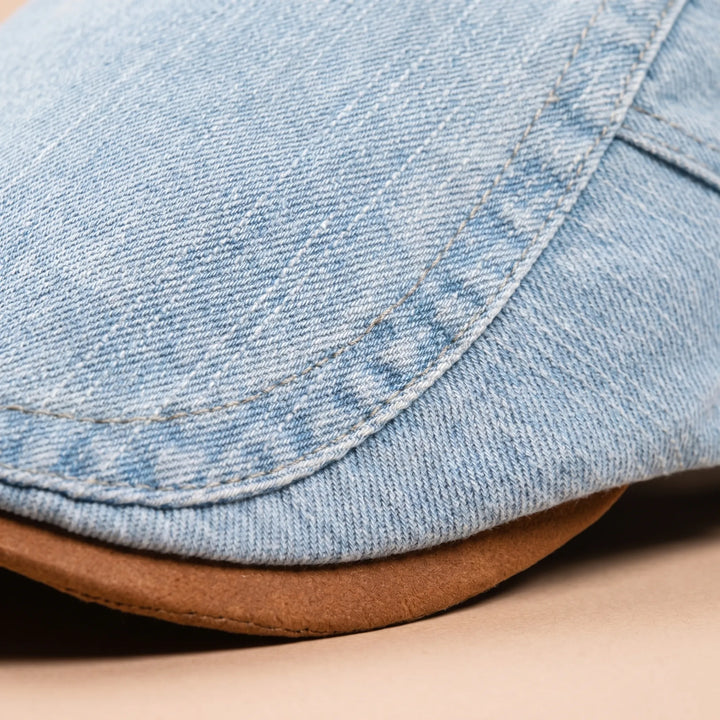 Gros plan sur le tissu denim délavé bleu clair, les surpiqûres et le bord de la visière brune. 4