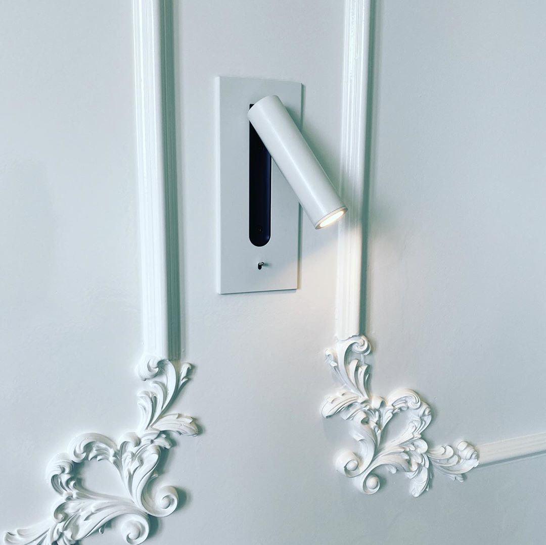Applique blanche installée sur un mur blanc à moulures ornementales, spot allumé 27