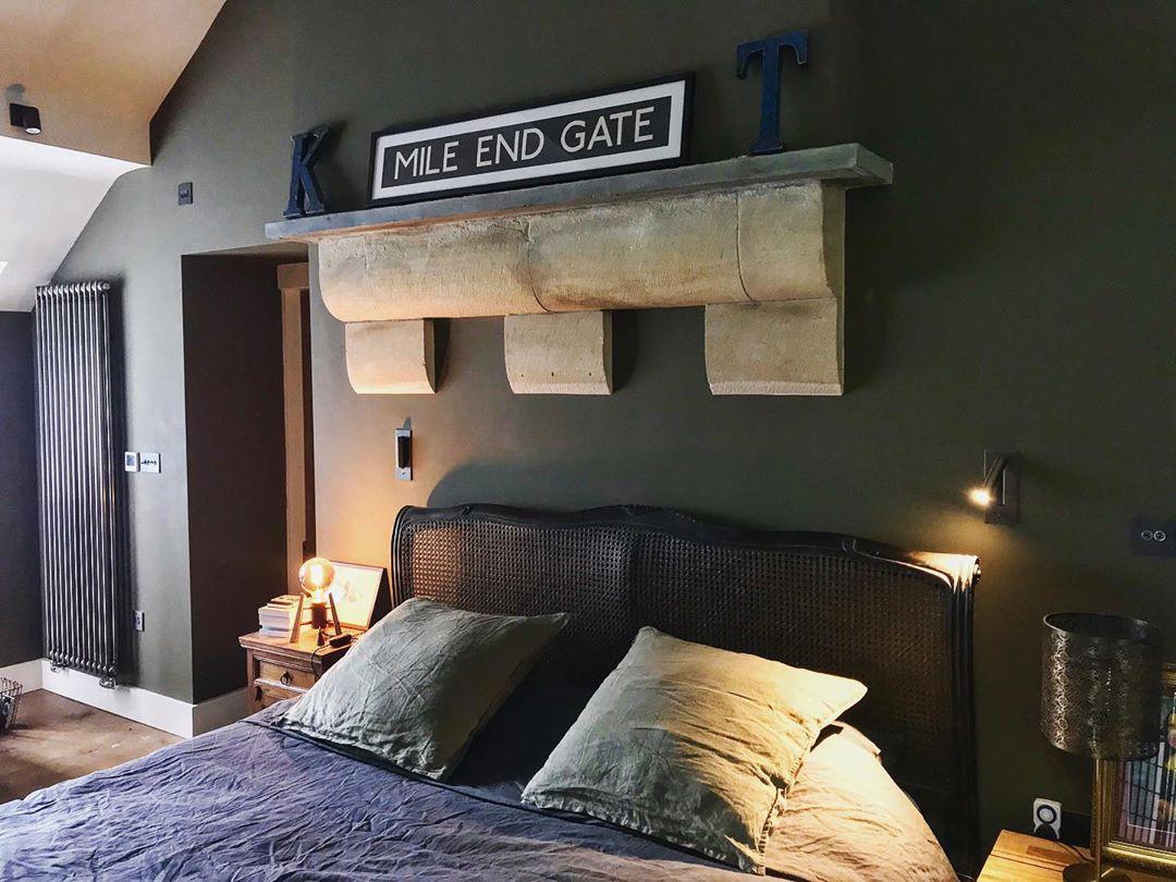 Deux appliques sur un mur vert foncé au-dessus d'un lit avec tête de lit cannée, l'une allumée 37