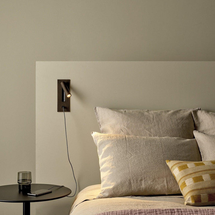 Applique bronze avec câble de recharge branché sur un téléphone posé sur une table de chevet 36