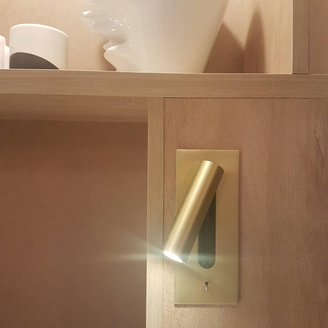 Applique dorée encastrée dans un meuble en bois clair, spot allumé près d'une étagère 32