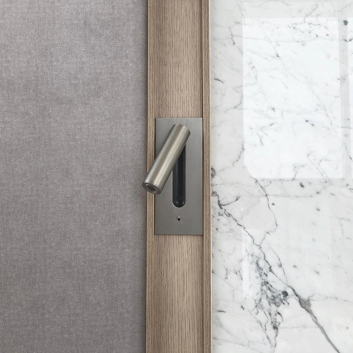 Applique en métal brossé, spot tourné vers la gauche, entre un mur en tissu gris et du marbre 33