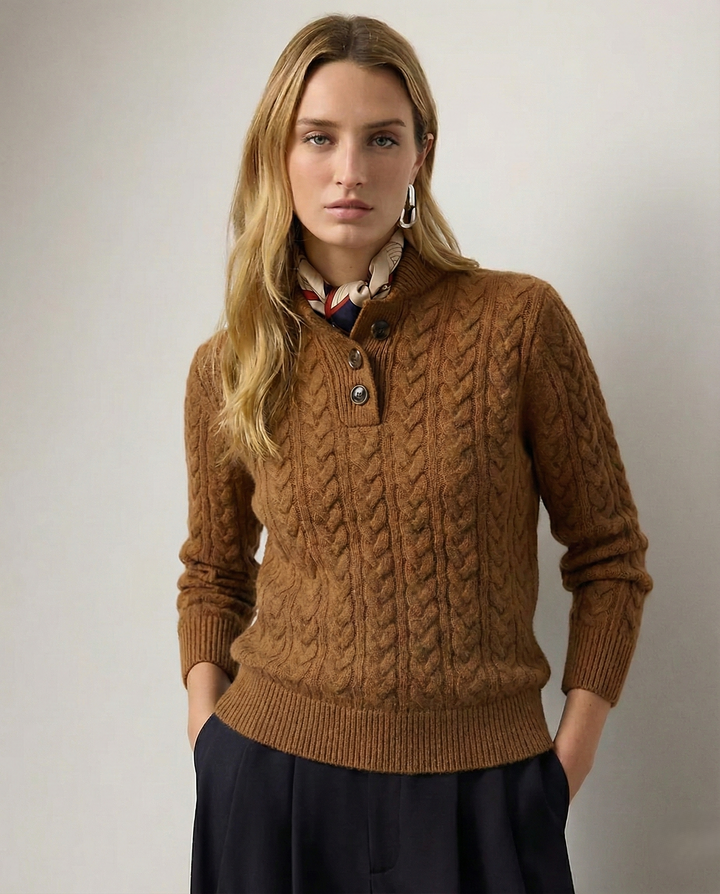 Femme de face portant le pull camel en maille torsadée à col boutonné, foulard au cou, pantalon sombre, mains dans les poches. 1