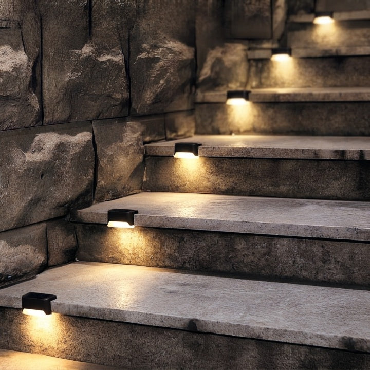 Lampes solaires noires encastrées sur des marches en pierre brute contre un mur rocheux, éclairant l'escalier d'une lumière chaude. 6