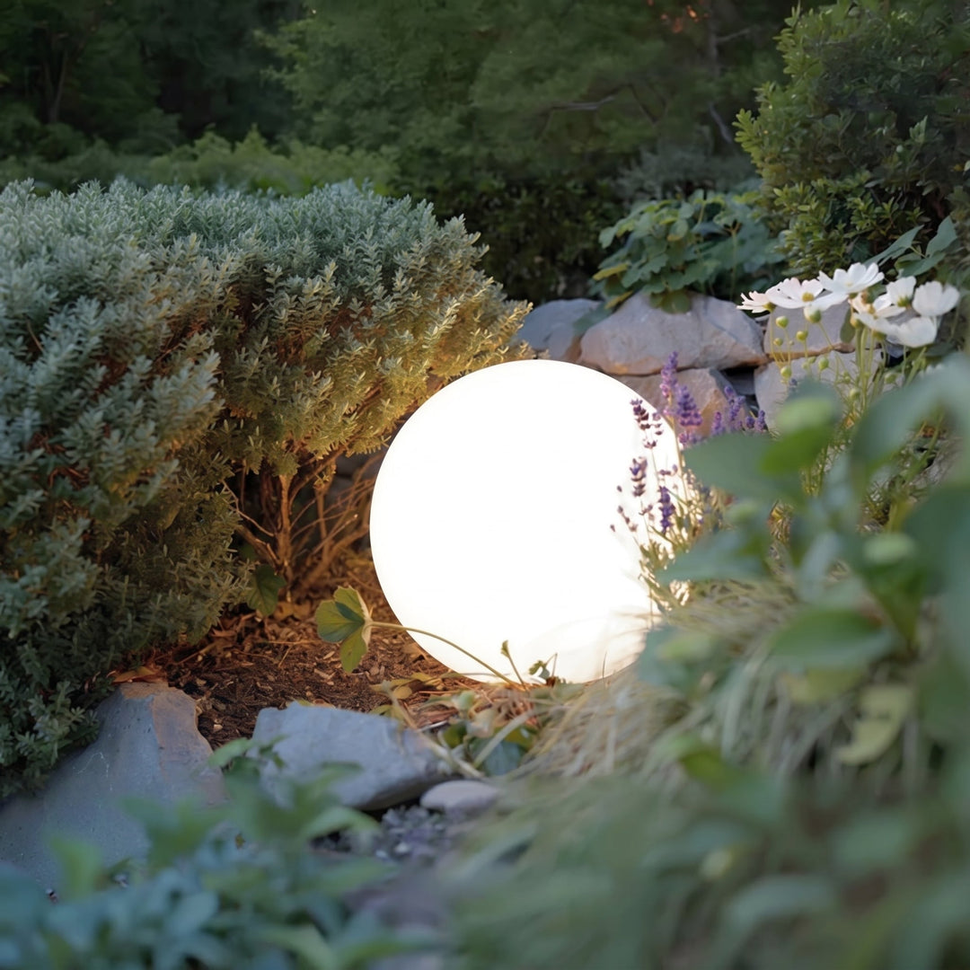 Gros plan sur une sphère lumineuse blanche posée au sol, nichée entre un arbuste, des pierres et des fleurs de lavande. 5