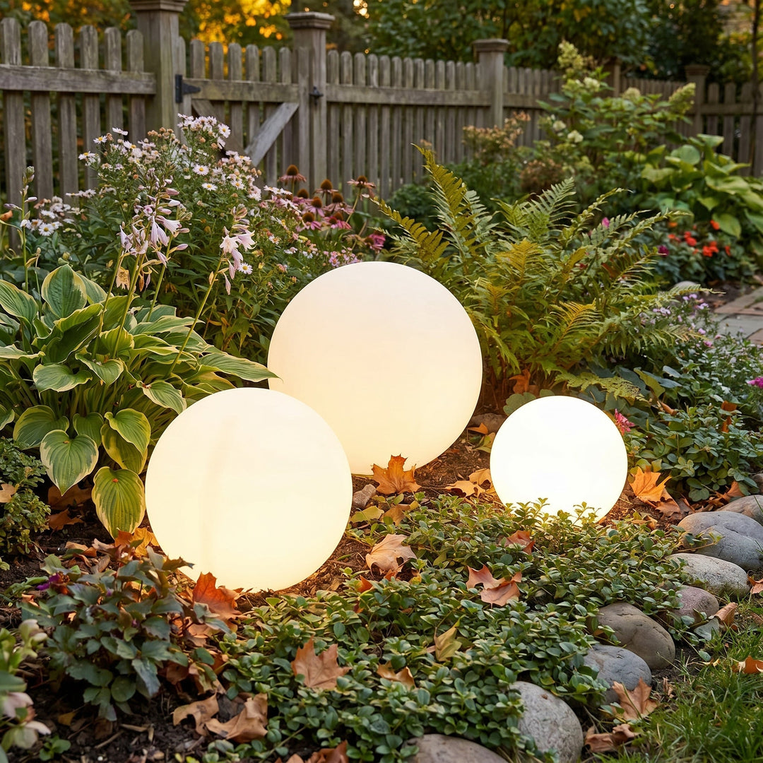 Trois sphères lumineuses de tailles différentes au milieu d'un massif de fleurs, de fougères et de feuilles d'automne, devant une clôture en bois. 2
