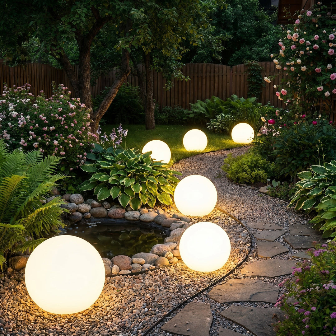 Rangée de sphères lumineuses bordant une allée de gravier et un petit bassin entouré de galets, dans un jardin fleuri le soir. 4
