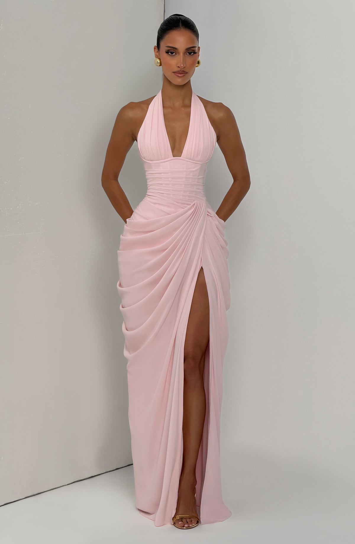 Robe rose pâle portée devant un mur gris clair, décolleté en V, taille corsetée et fente haute. 8