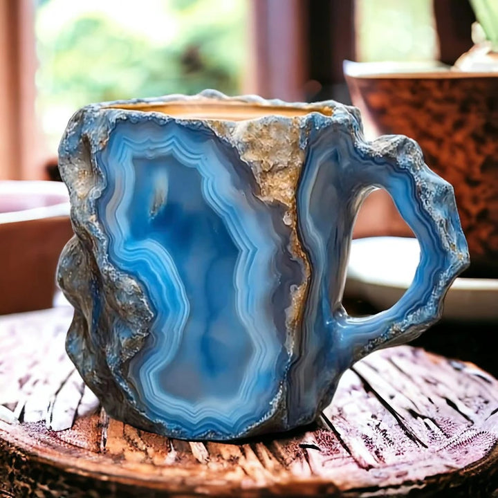 Tasse bleue aux veines d'agate blanches et bords rocheux irréguliers, anse sculptée, posée sur une planche de bois rustique. 1