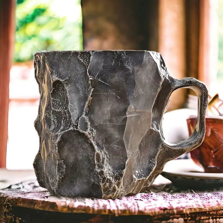 Tasse grise taillée à facettes comme une roche brute, anse à droite, posée devant une fenêtre lumineuse. 4
