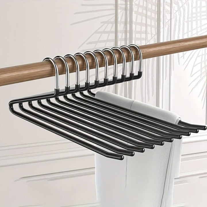 Série de cintres noirs accrochés à une tringle en bois, avec un pantalon blanc suspendu 1