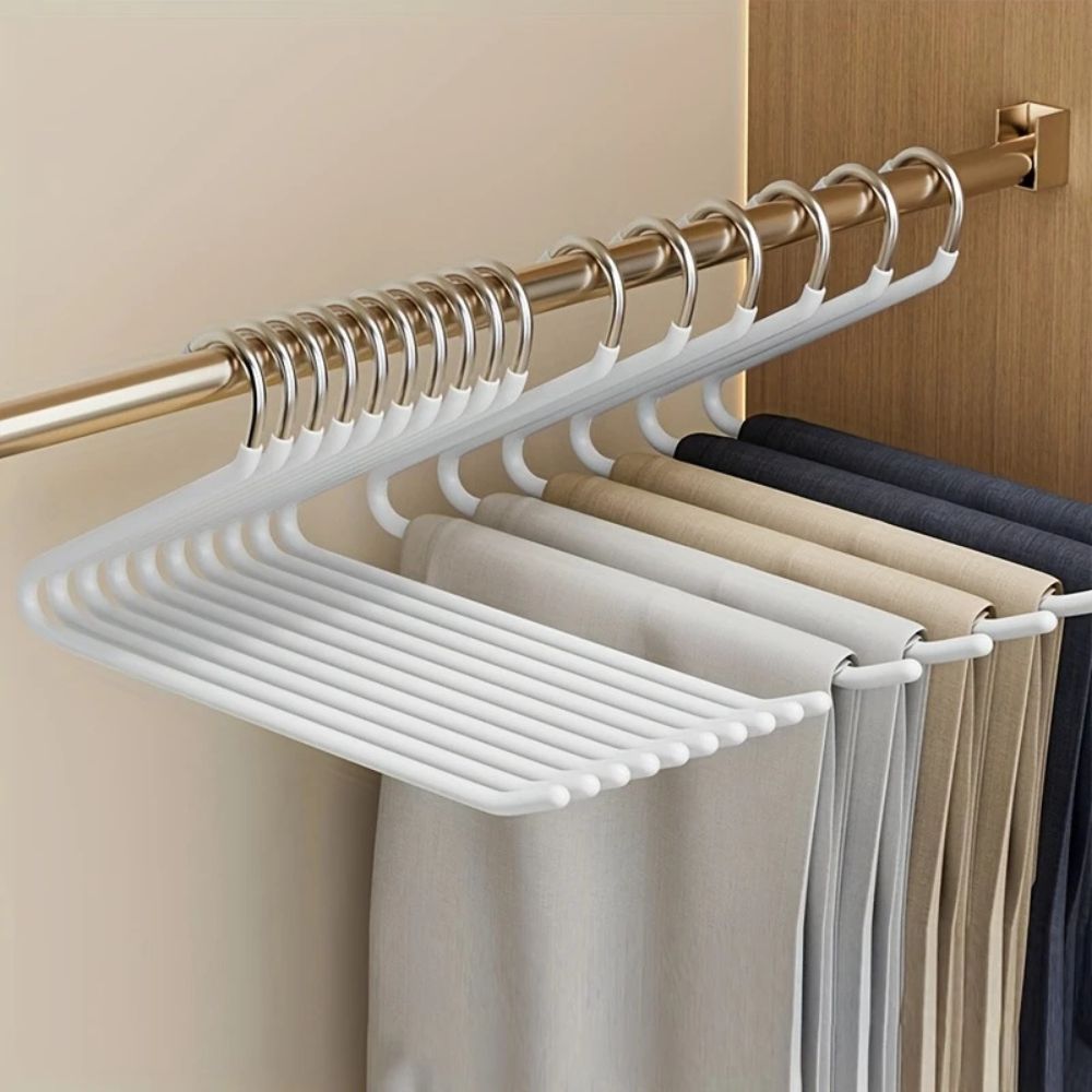 Cintres blancs alignés sur une tringle dorée de placard, portant plusieurs pantalons beiges, gris et bleu foncé 3