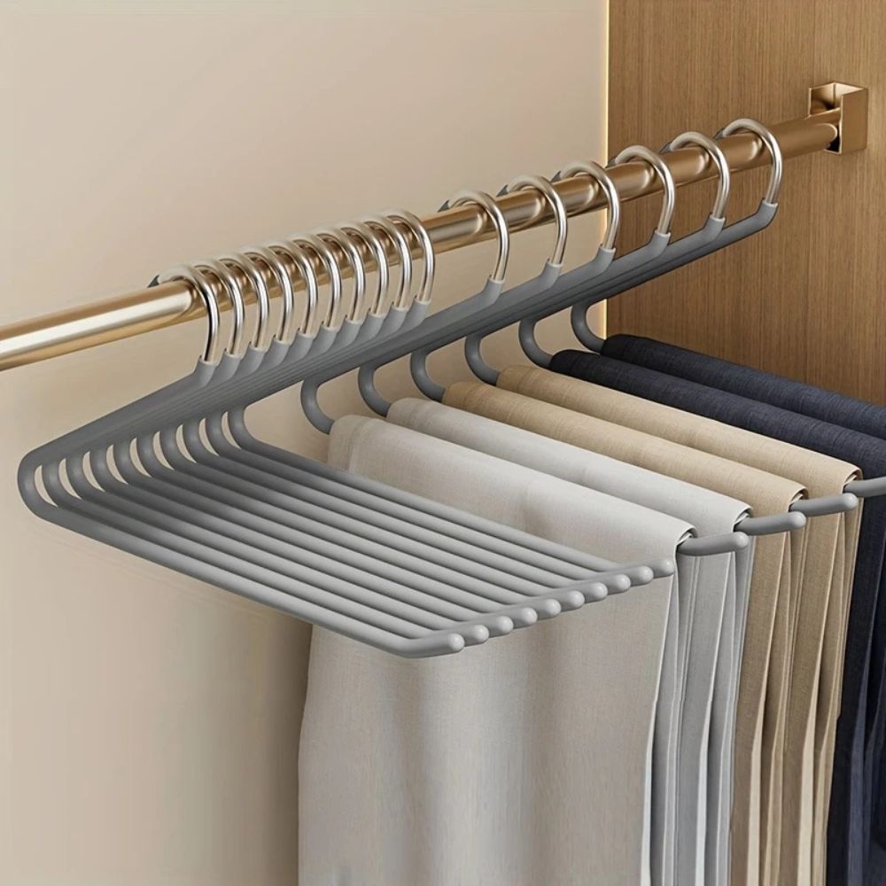 Cintres gris alignés sur une tringle dorée de placard, portant plusieurs pantalons beiges, gris et bleu foncé 4