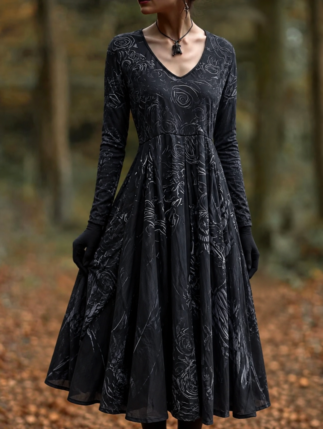Femme en forêt d'automne portant la robe noire évasée à col en V et manches longues, ornée de motifs gris, gants noirs et collier. 1