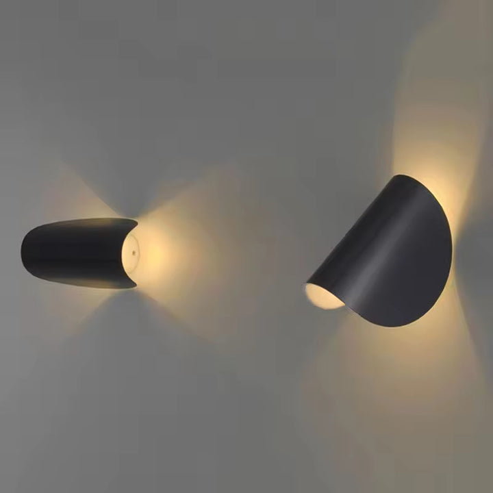 Deux appliques noires orientées différemment, l'une de profil et l'autre inclinée, projetant une lumière dorée sur un mur gris. 2