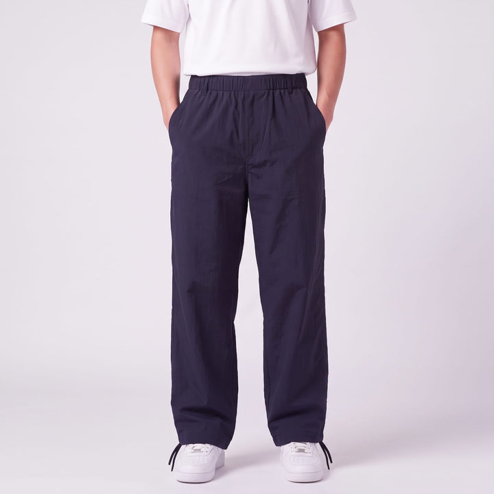 Vue de face du pantalon bleu marine à taille élastique, porté mains dans les poches avec un t-shirt blanc et des baskets blanches. 1