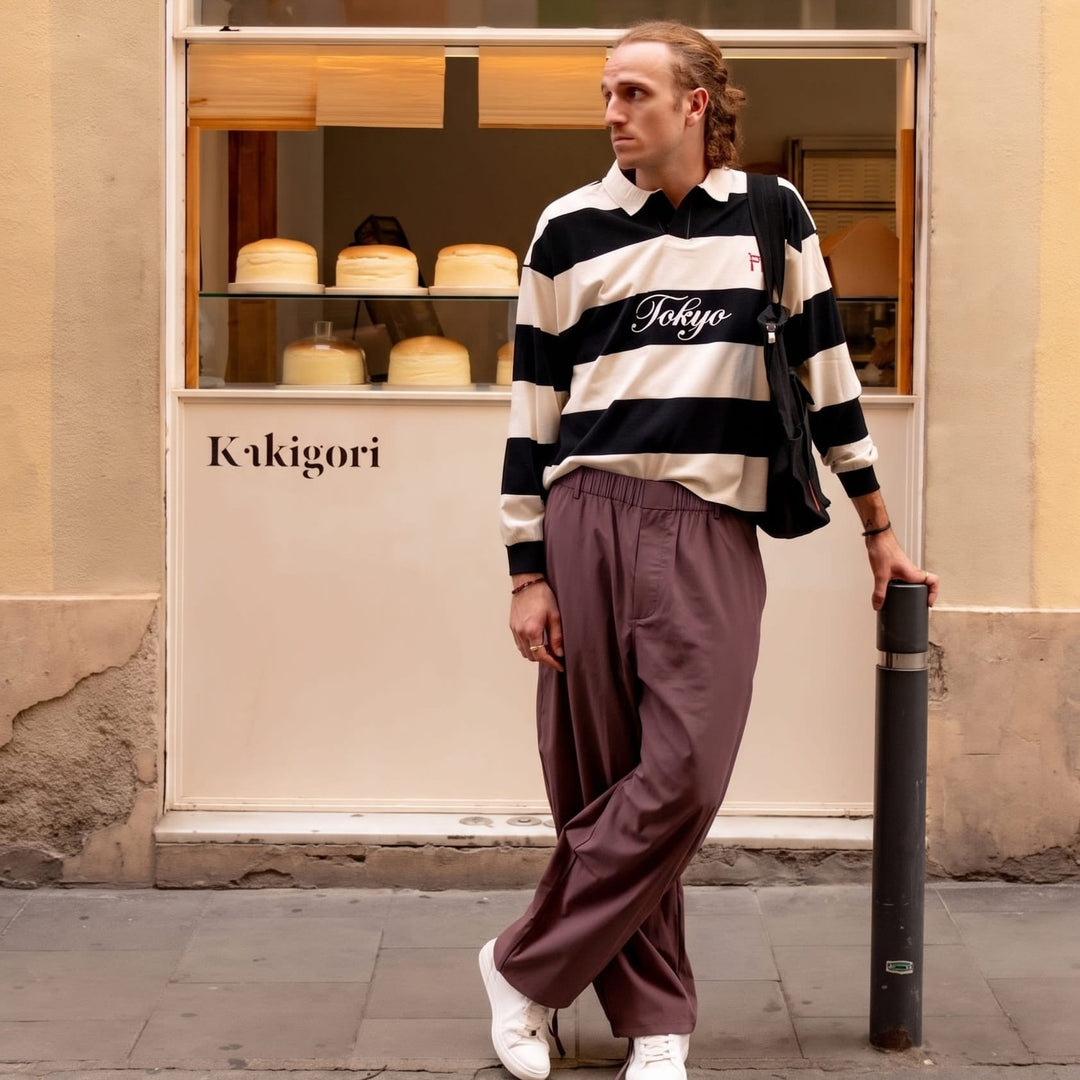 Homme appuyé contre une vitrine de pâtisserie, portant le pantalon ample prune à taille élastique avec un polo rayé noir et blanc. 3