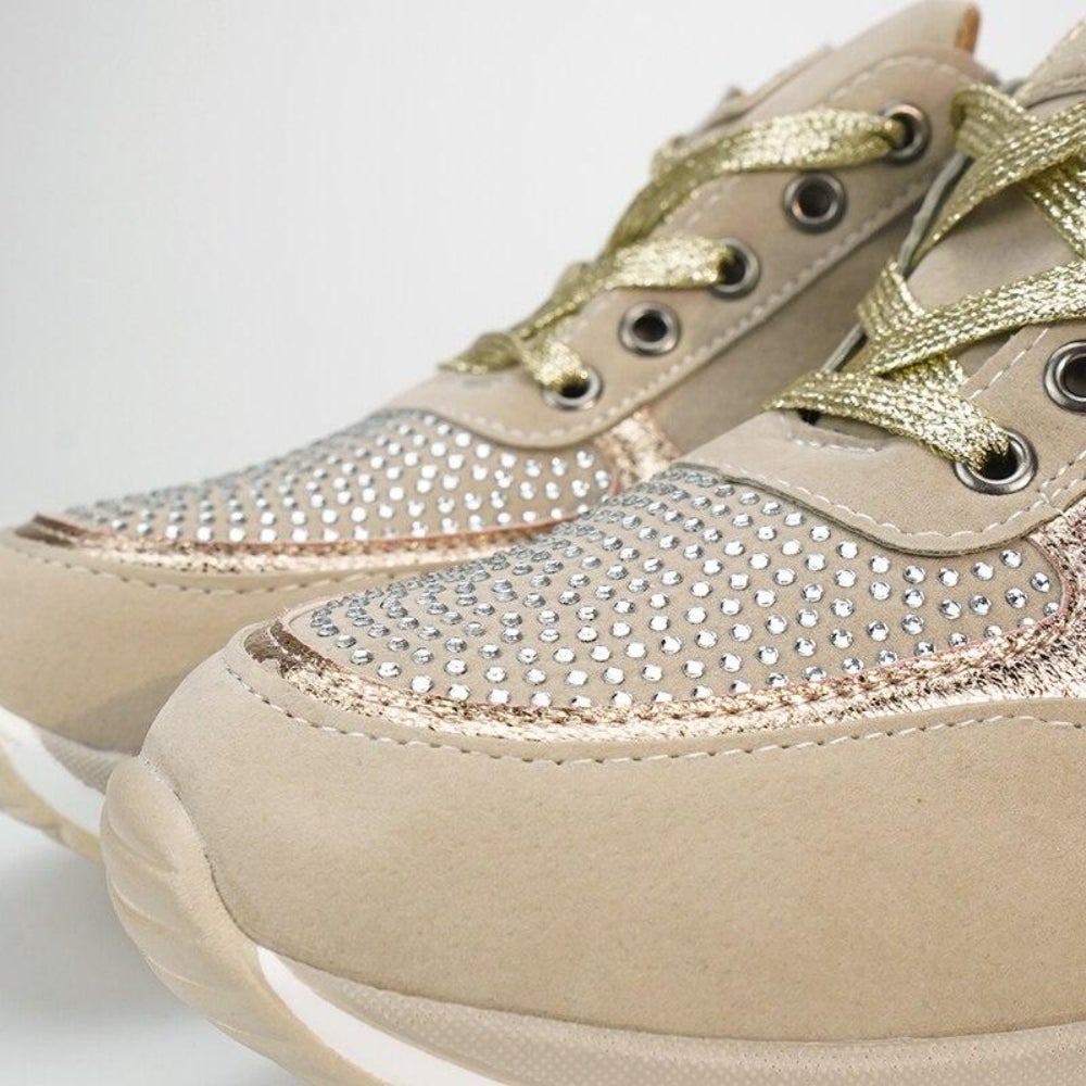 Gros plan sur le bout des baskets beiges avec strass sur l'empeigne, lacets dorés et semelle blanche épaisse. 10
