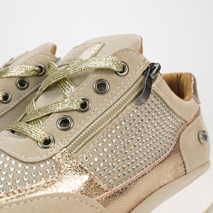 Gros plan sur les lacets dorés, les œillets métalliques, le zip latéral et les strass d'une basket beige. 8
