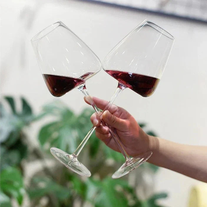 Une main tient deux verres de vin rouge inclinés qui trinquent, devant des plantes vertes 7