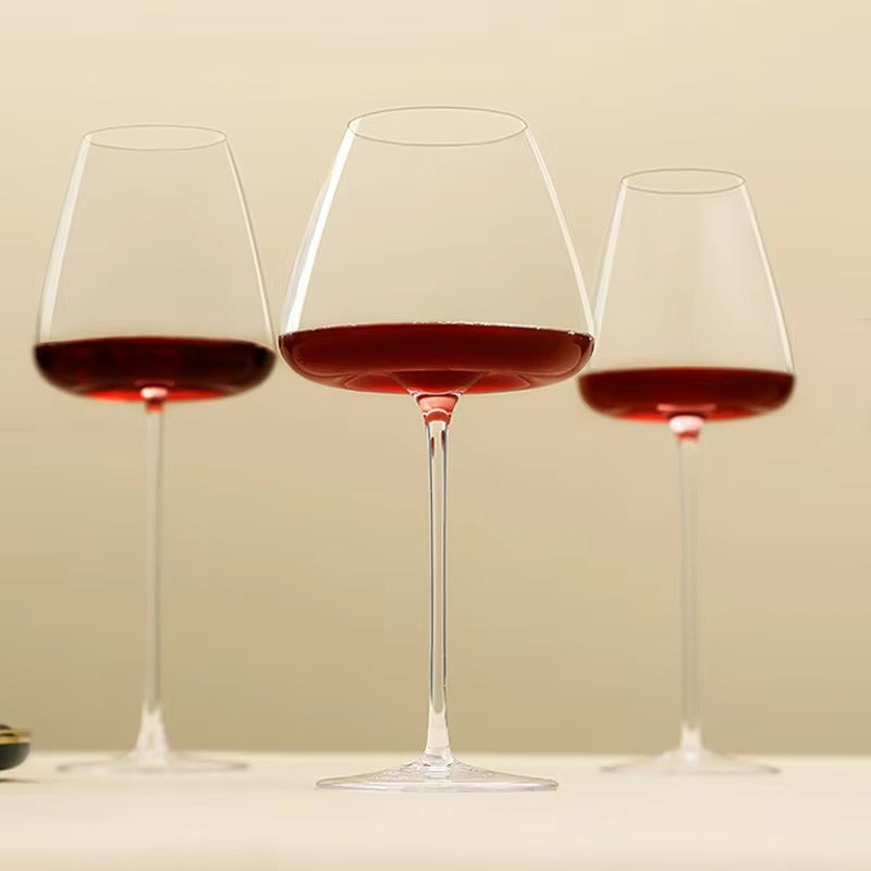Trois verres à vin rouge à pied fin alignés sur fond beige, vus de près 10