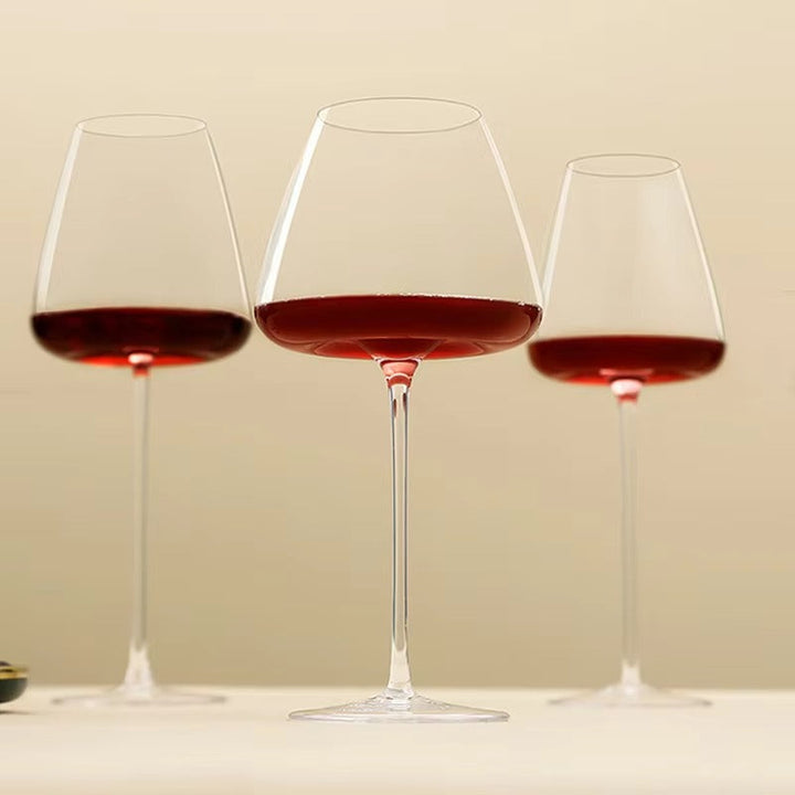 Trois verres à vin rouge à pied fin alignés sur fond beige, vus de près 10