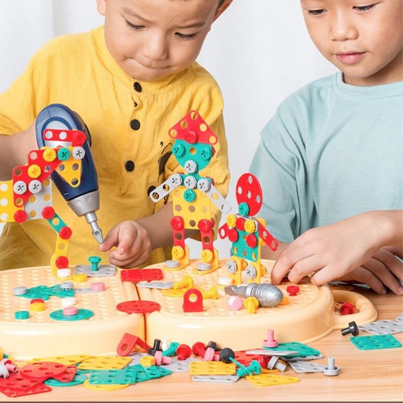 Deux enfants jouent ensemble à assembler des robots colorés sur la plaque de jeu, l'un tenant la perceuse jouet bleue. 3