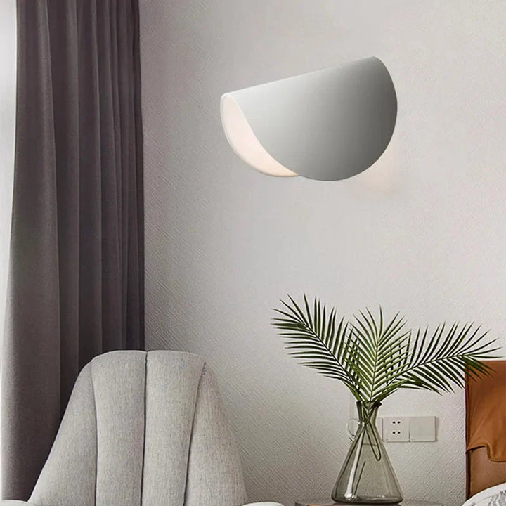 Applique blanche inclinée dans un salon, au-dessus d'un vase en verre avec des palmes, près d'un fauteuil gris et d'un rideau. 9