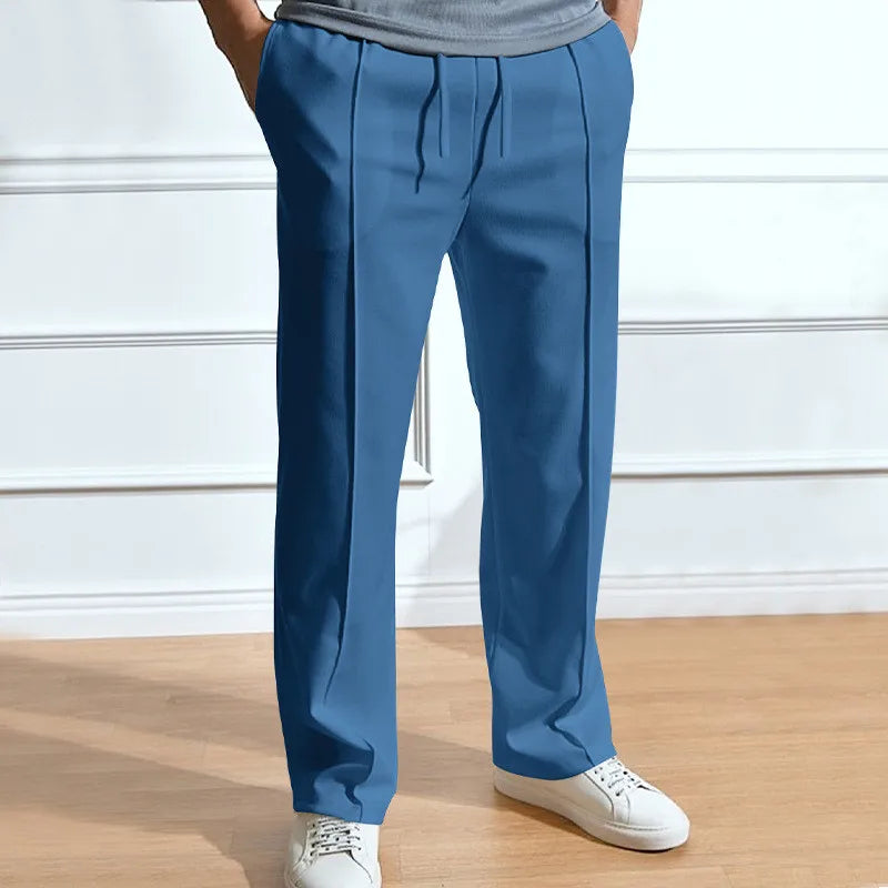 Pantalon bleu denim à taille élastique et plis marqués, porté avec un t-shirt gris et des baskets blanches. 5